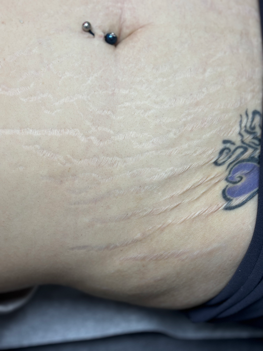 A close up of a woman 's stomach with a tattoo and a piercing.