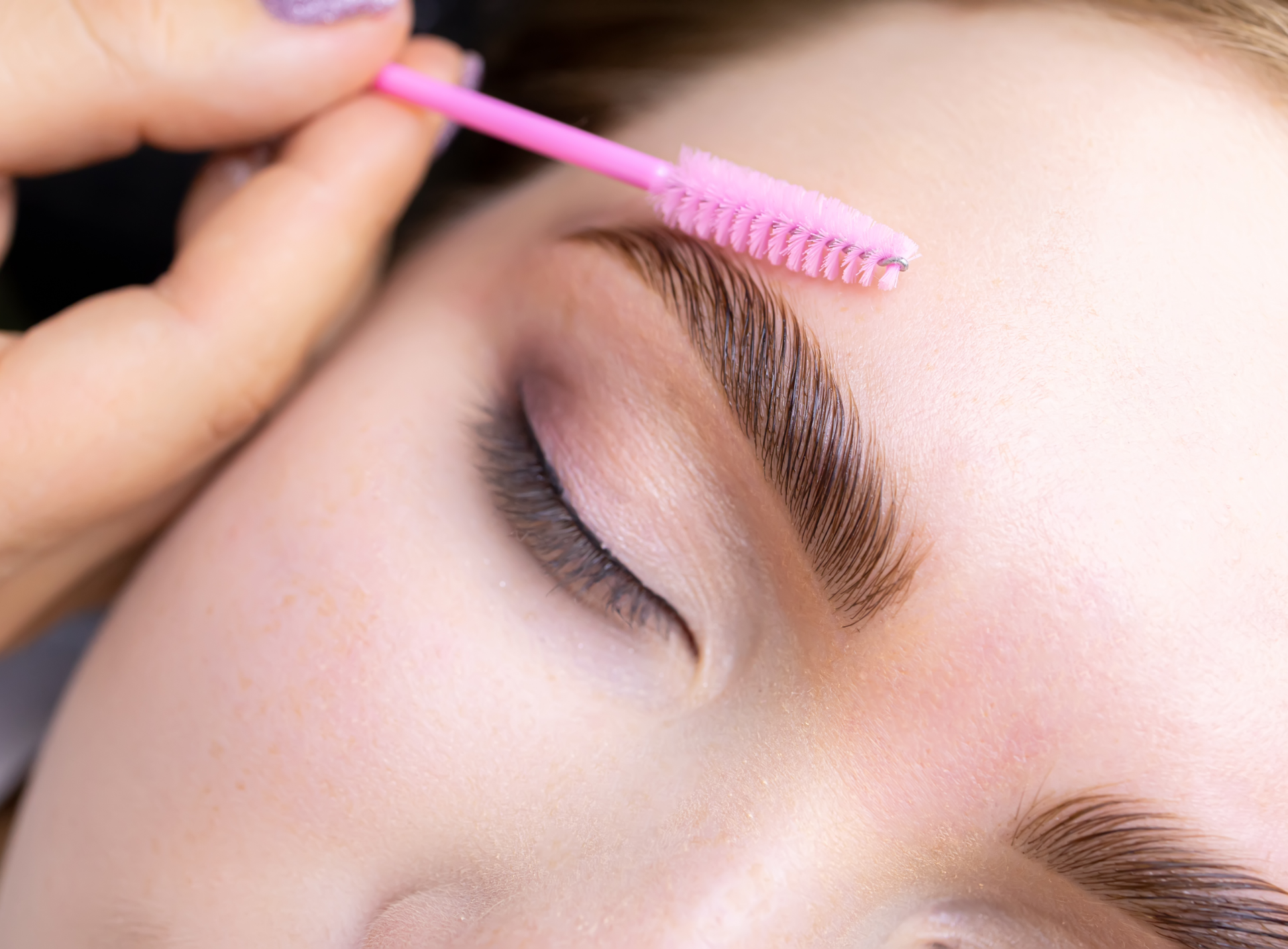 A woman is getting her eyebrows done by a makeup artist.