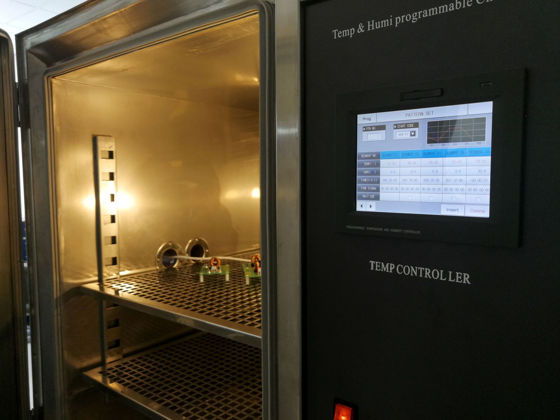 Environmental test chamber with digital controls and sample components on metal shelves.