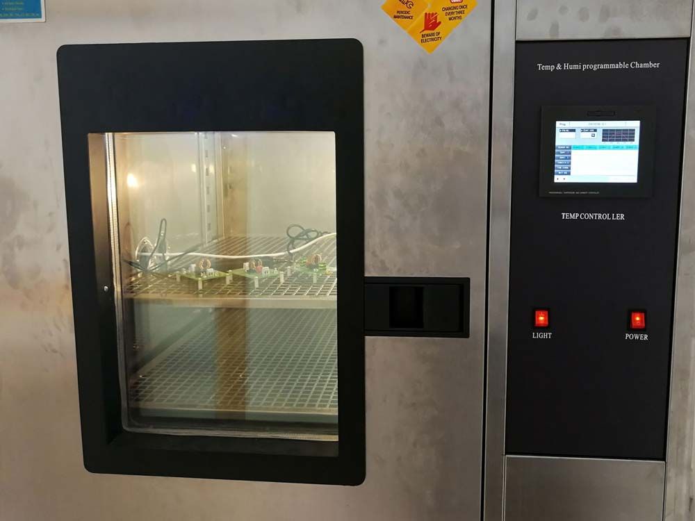 Environmental test chamber with a viewing window and samples placed on metal shelves.