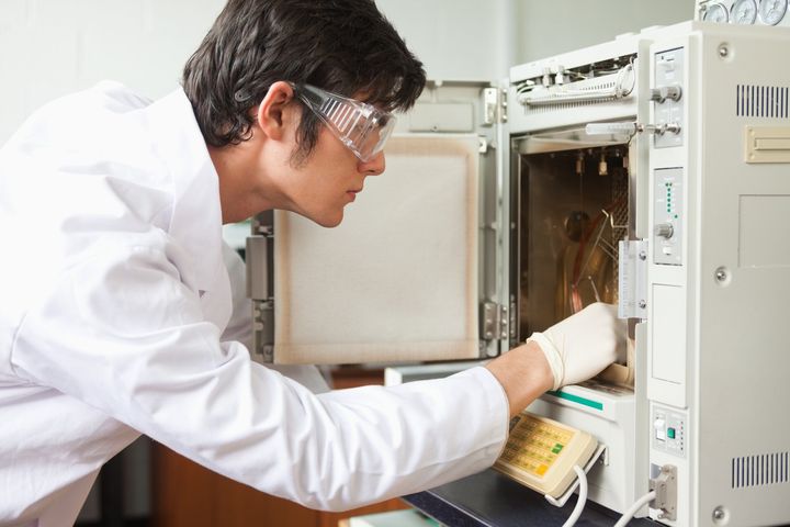A person wearing goggles and white coat looking at an open microwave.