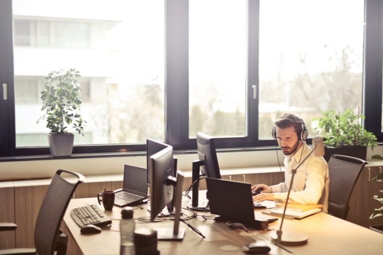 Een man met een koptelefoon zit aan een bureau voor een computer.