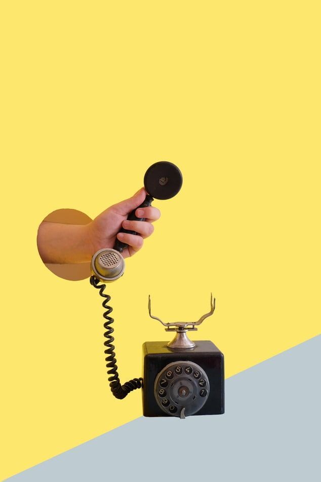 A hand is sticking out of a hole in a wall holding a telephone.