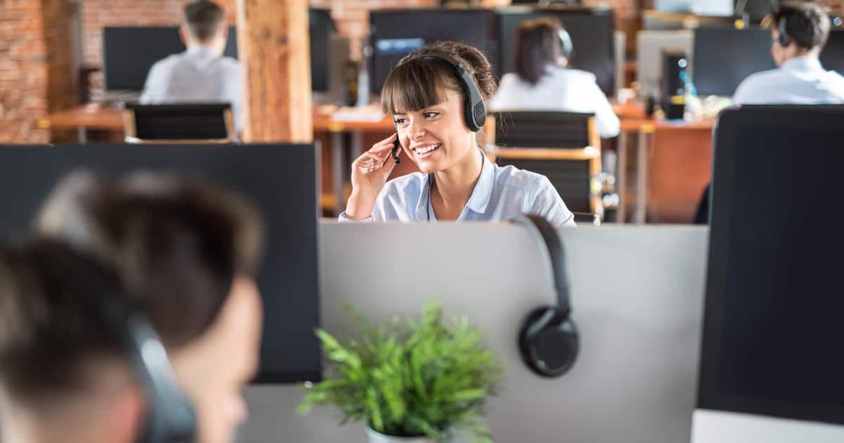 Een vrouw met een koptelefoon op praat met een mobiele telefoon in een callcenter.