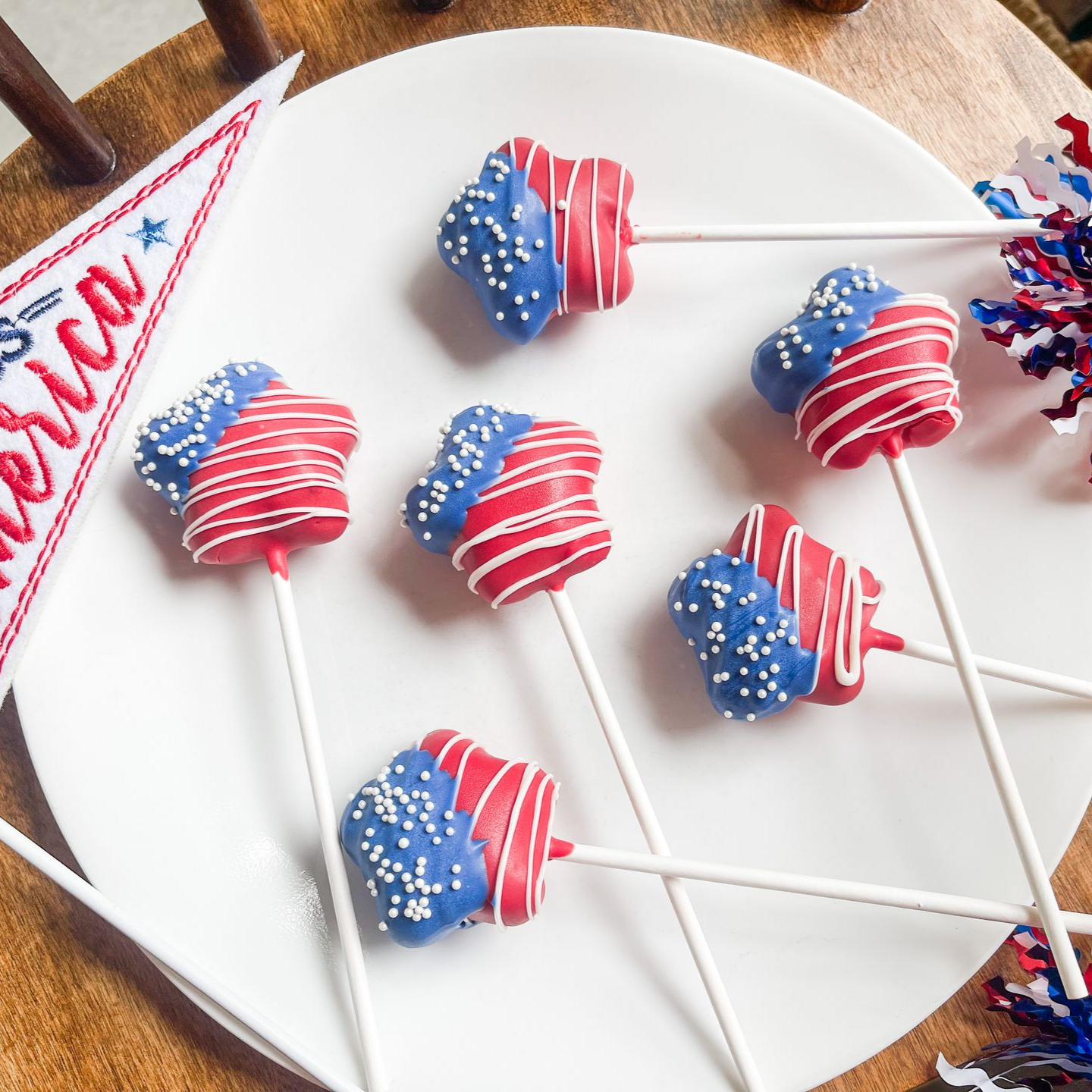 Star-shaped cake pops with red, white, and blue decoration arranged on a white plate, with a festive pennant nearby.