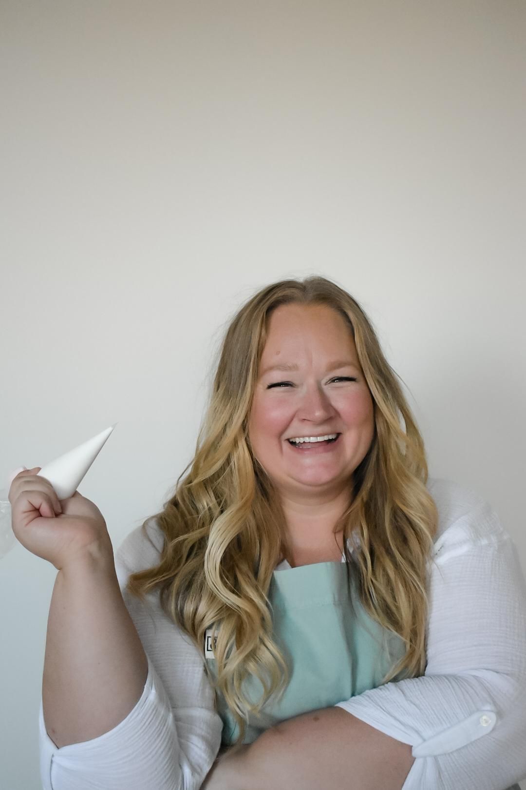 Woman in apron smiling, holding icing bag.