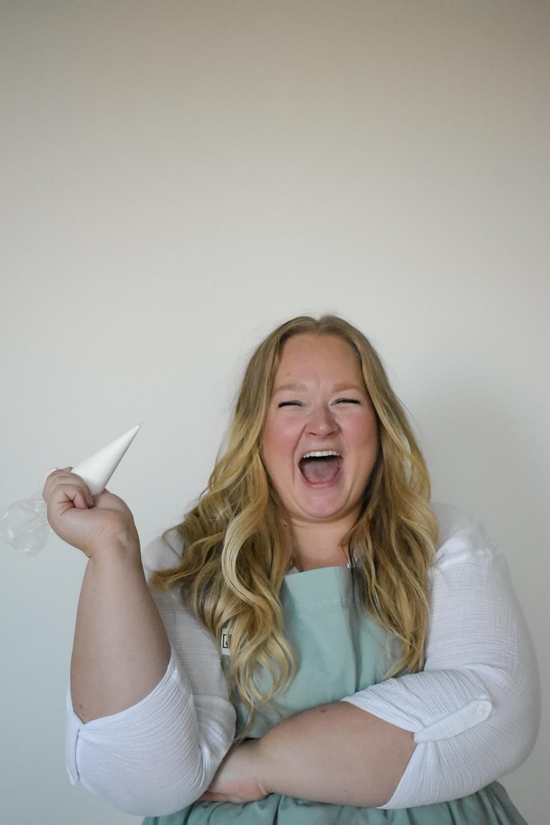 Woman in apron, laughing and holding pastry bag.