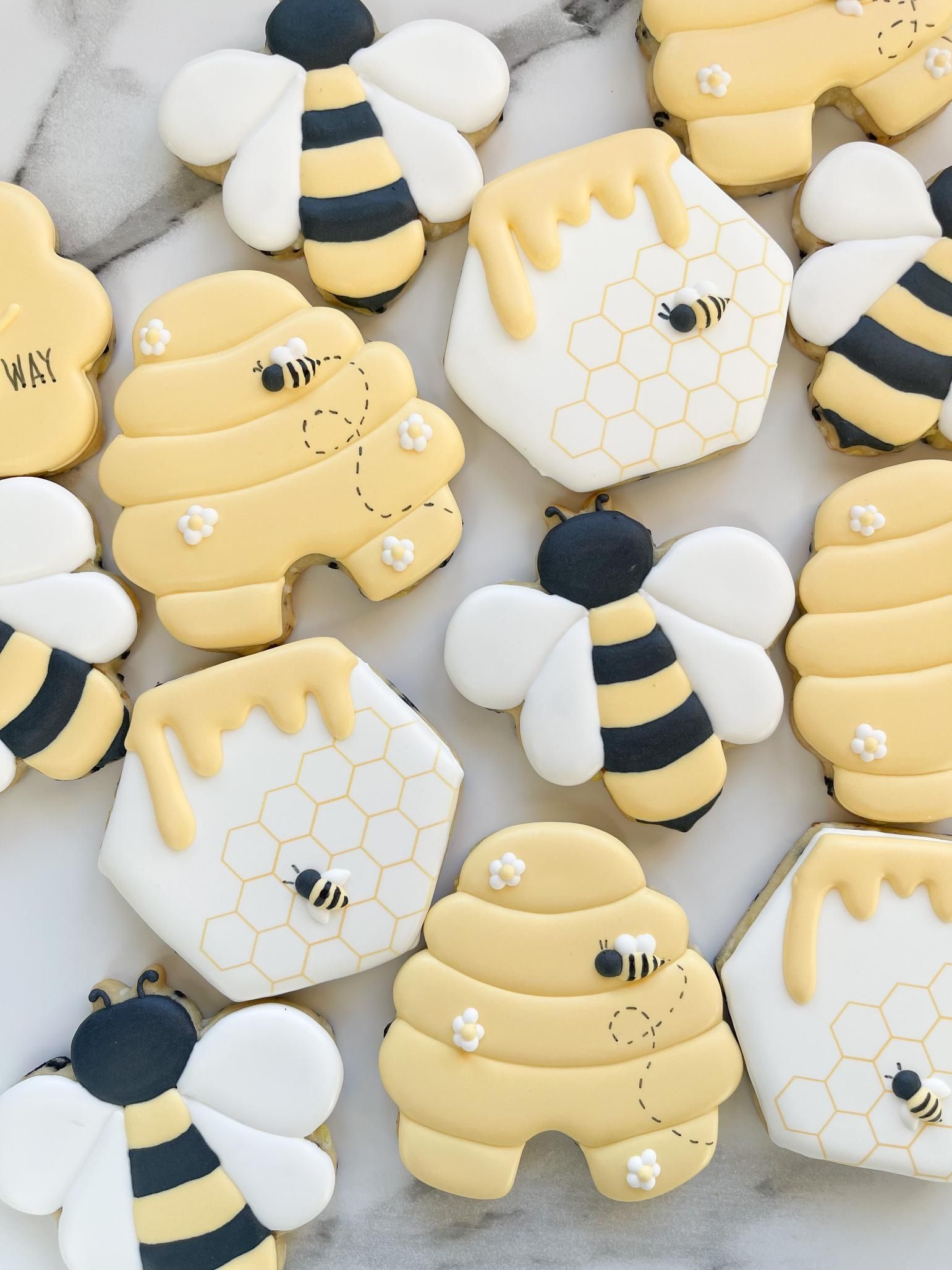 Decorated bee and honeycomb sugar cookies on a white surface, featuring yellow, black, and white frosting.