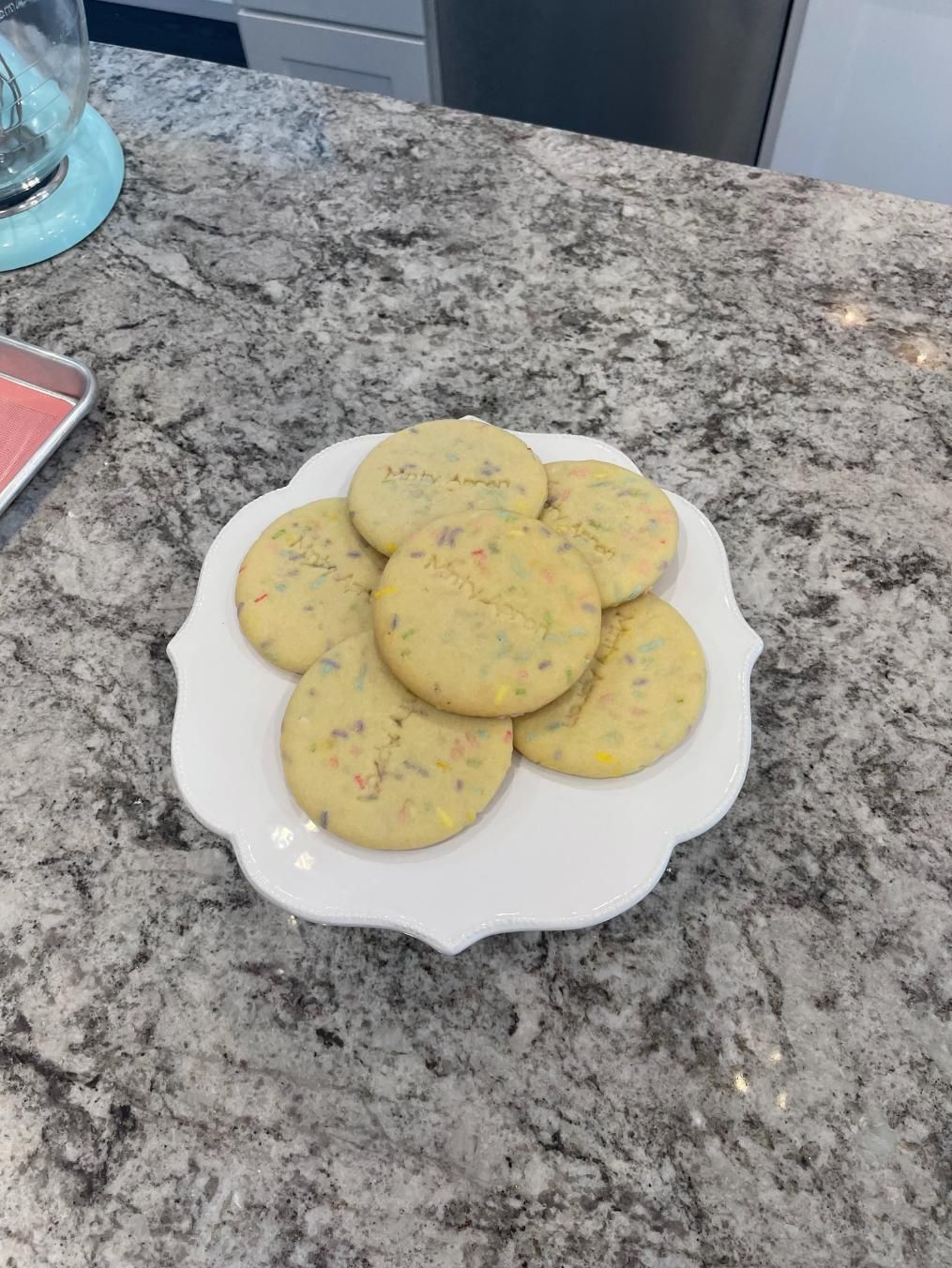 Cookies on a white, scalloped plate on a granite countertop. Several sprinkles are visible in the cookies.