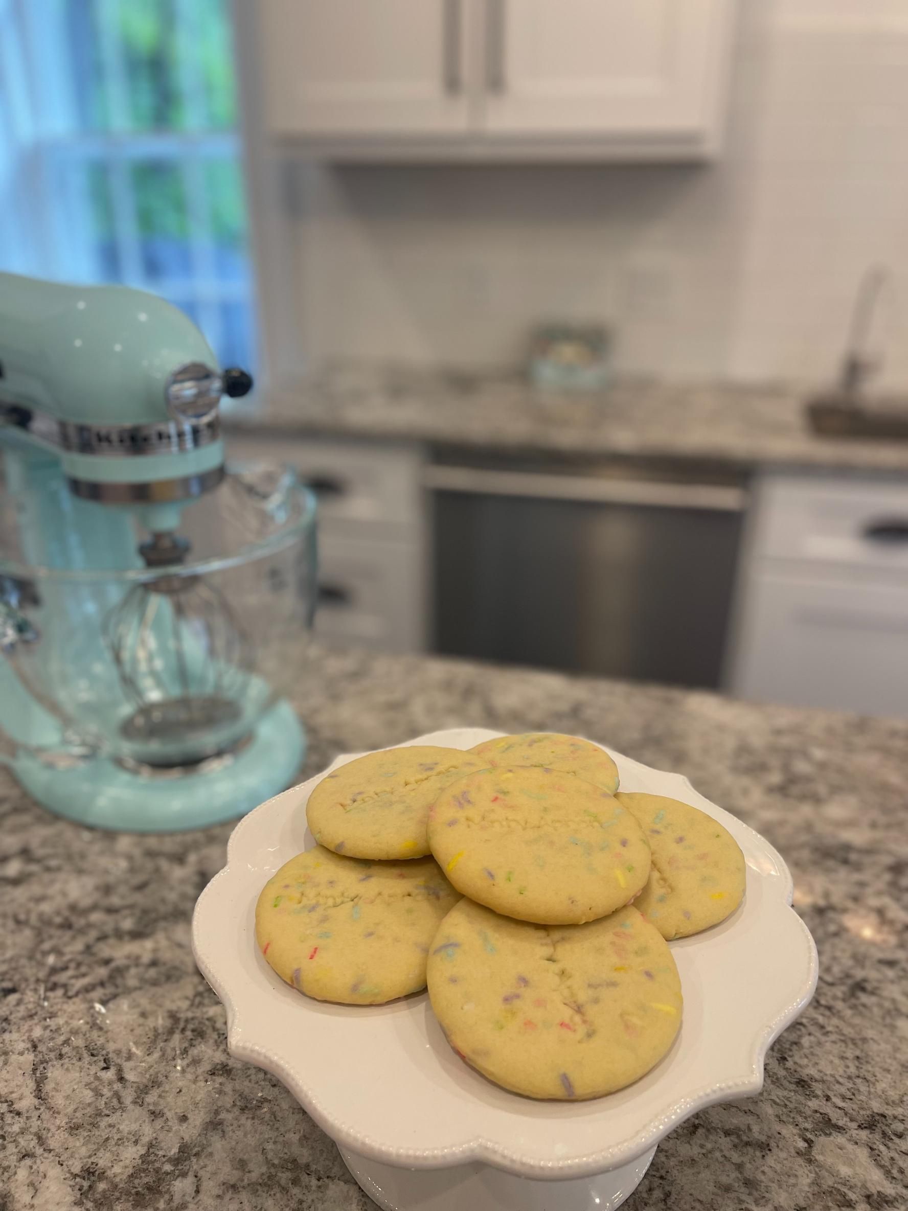 Cookies on a white cake stand in a kitchen with a blue stand mixer.