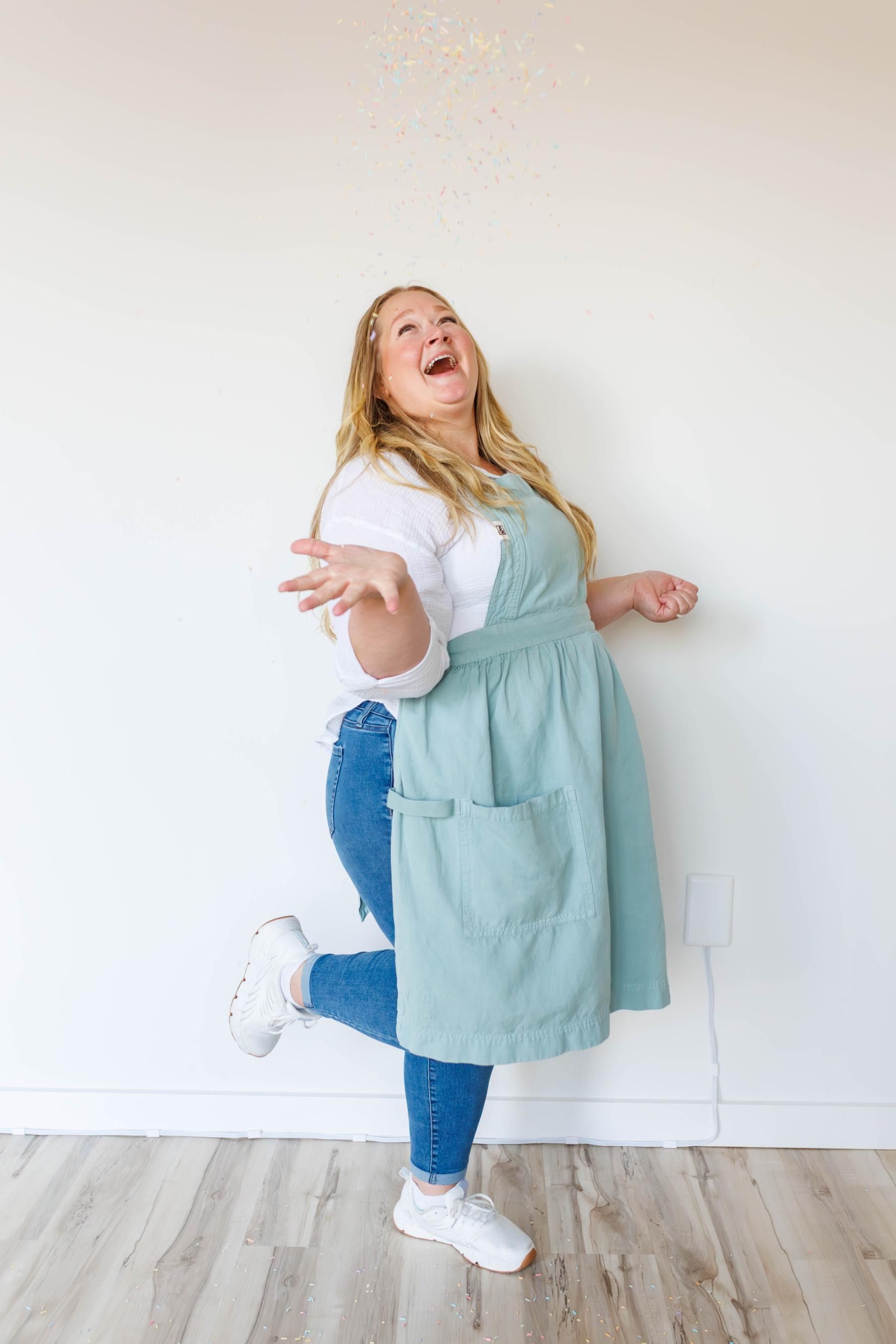 Woman in apron laughs, throwing flour upwards.