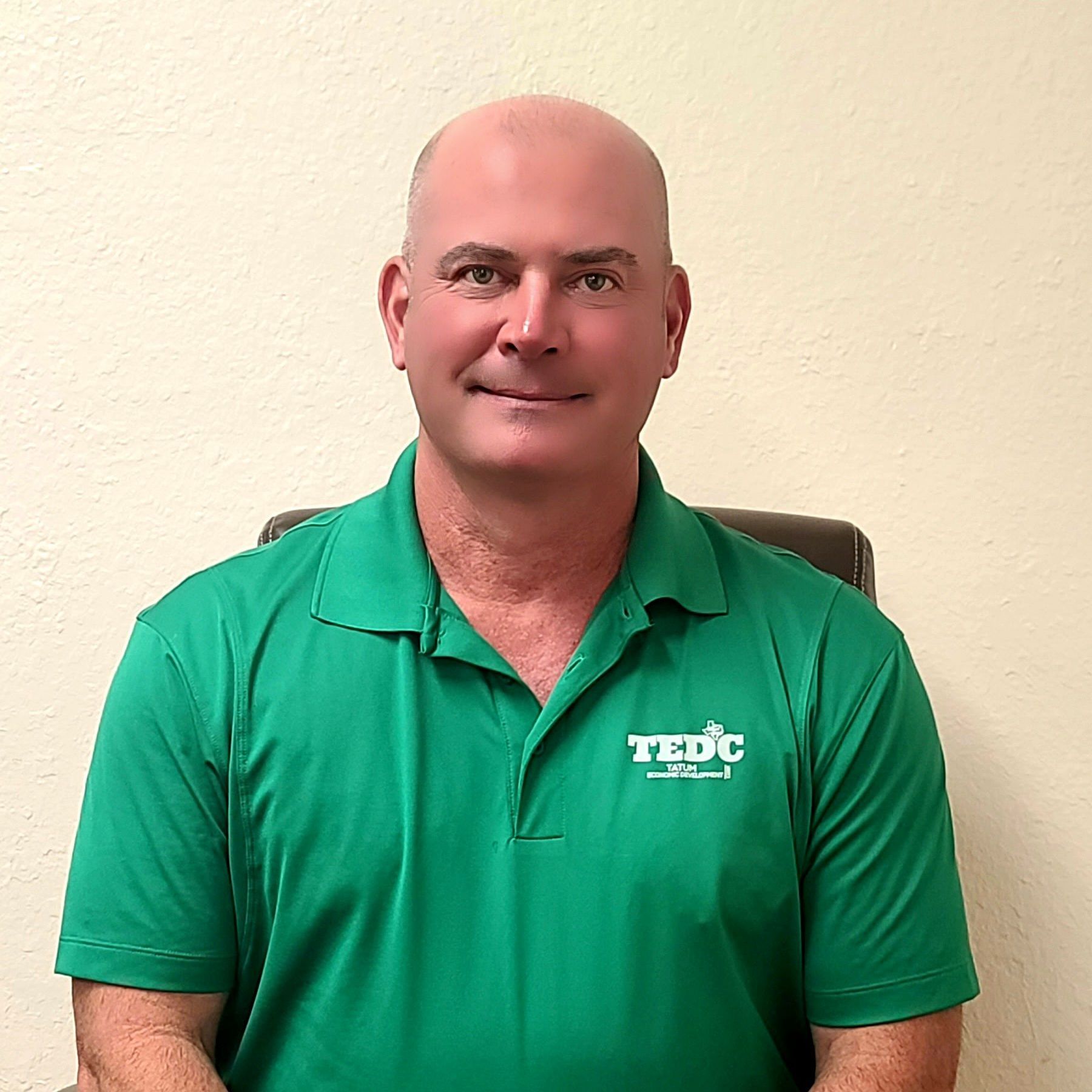 A bald man wearing a green polo shirt is sitting in a chair.