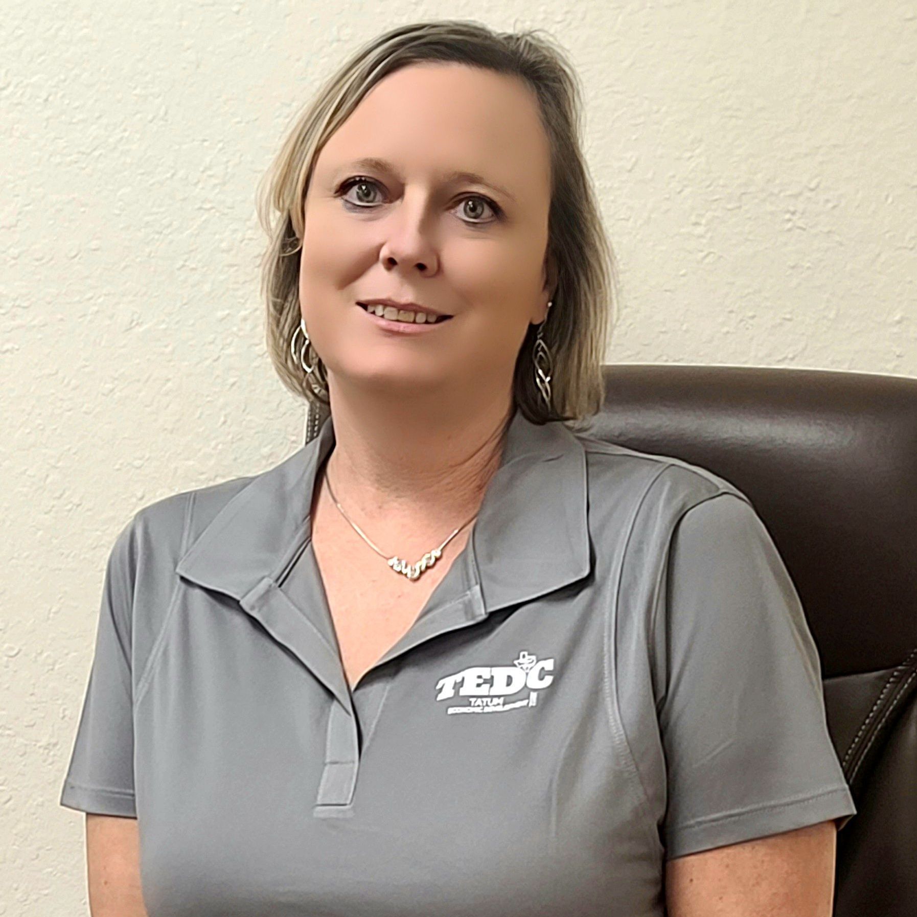 A woman is sitting in a chair wearing a gray shirt and a necklace.