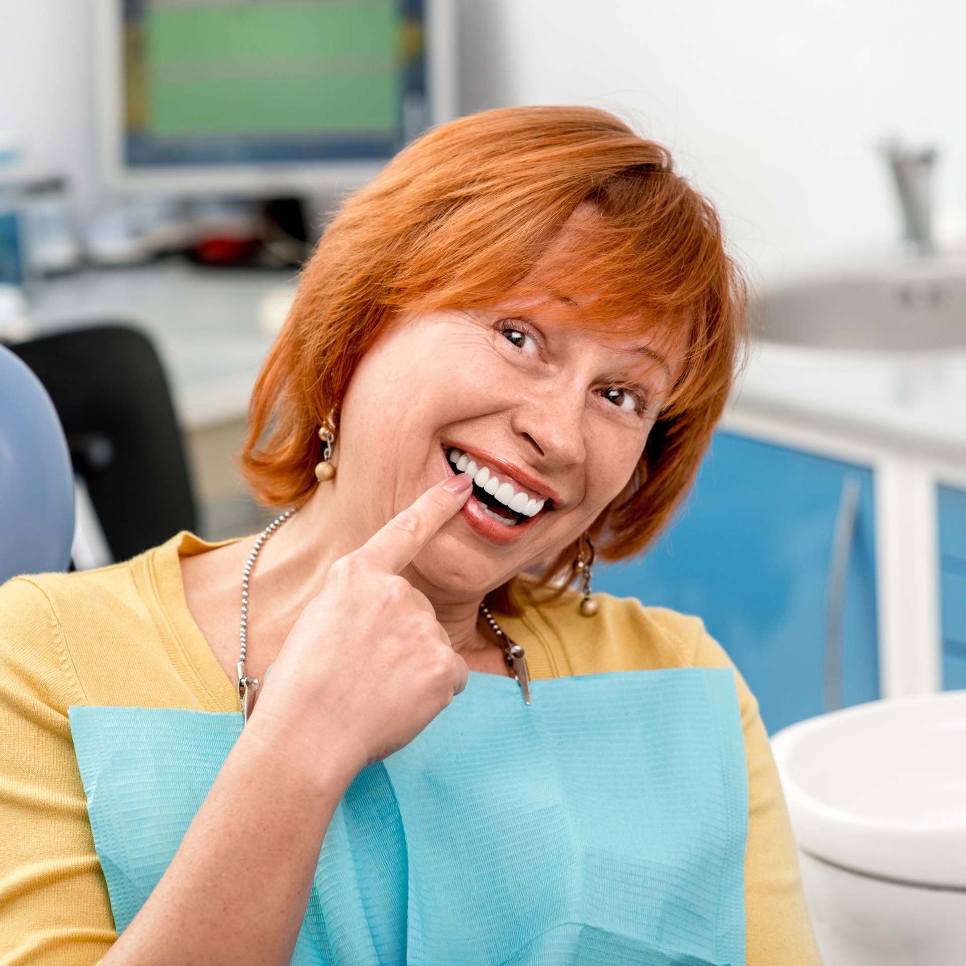 A woman with red hair is smiling and pointing at her teeth