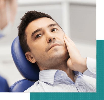 A man is sitting in a dental chair with his hand on his face.