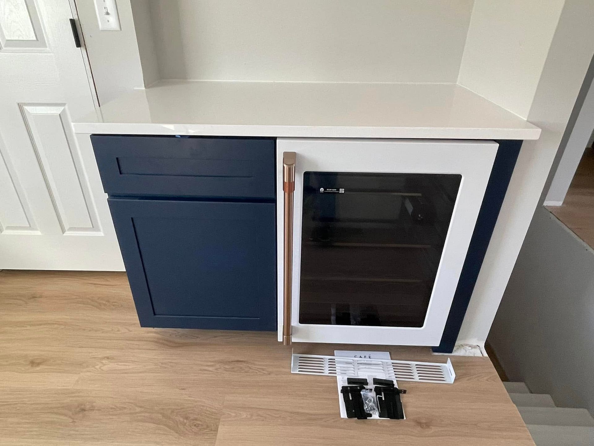 Blue cabinet with a built-in black and white wine cooler, white countertop, on wood flooring.