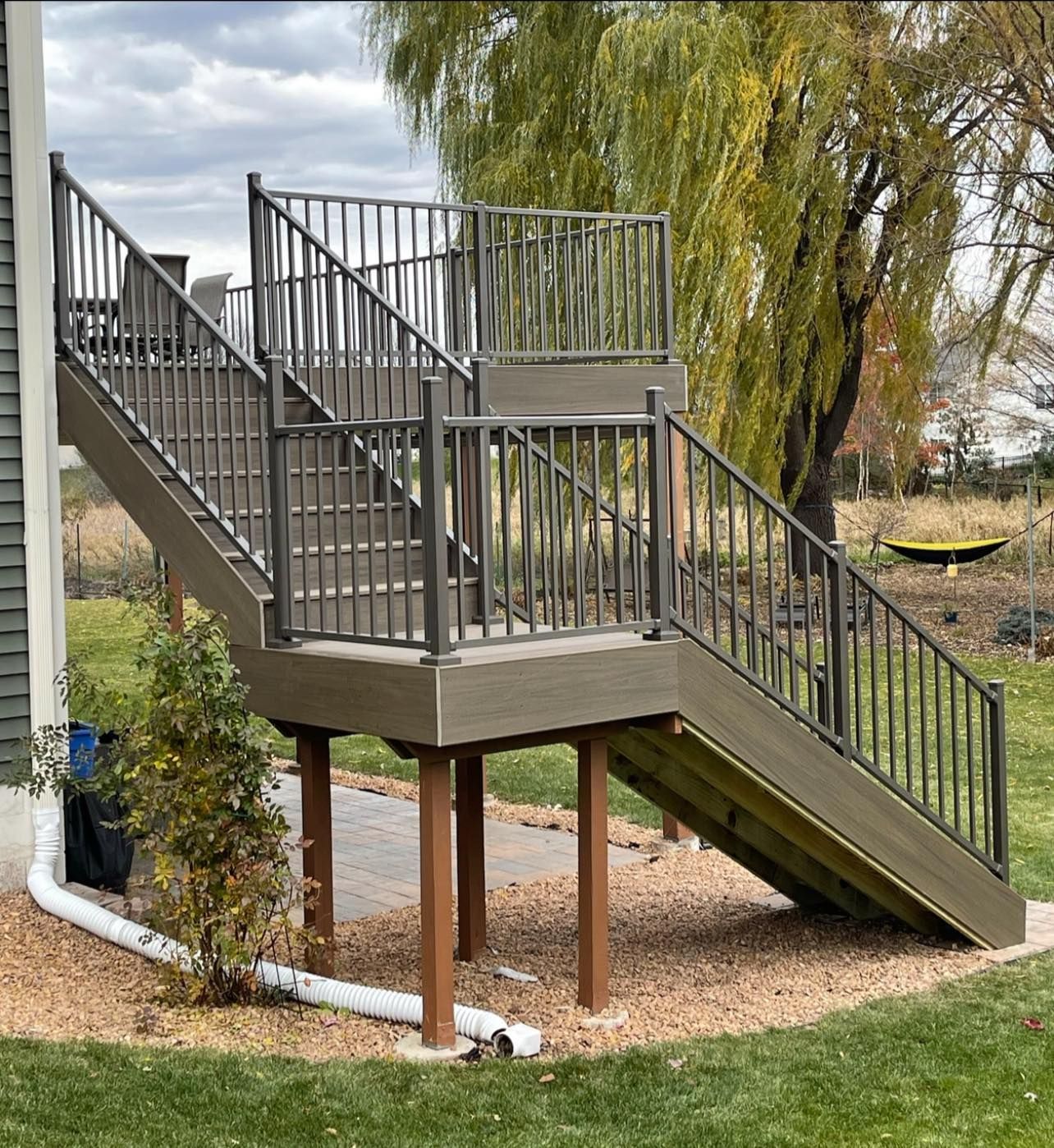 Composite deck with stairs and metal railing, supported by wooden posts, in a grassy yard.