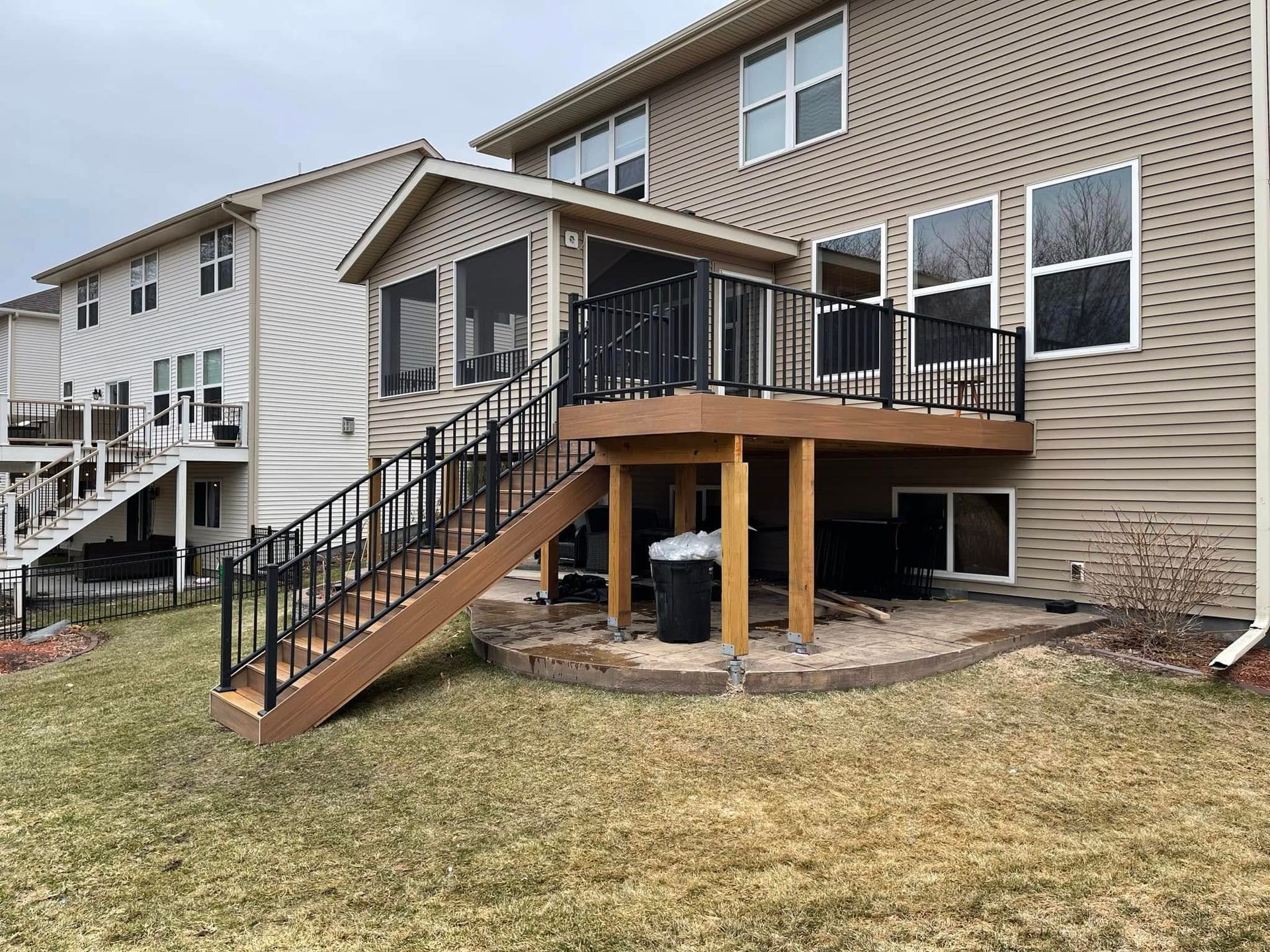 Backyard deck with black railings and stairs, connected to a beige house, overlooking a grassy lawn.