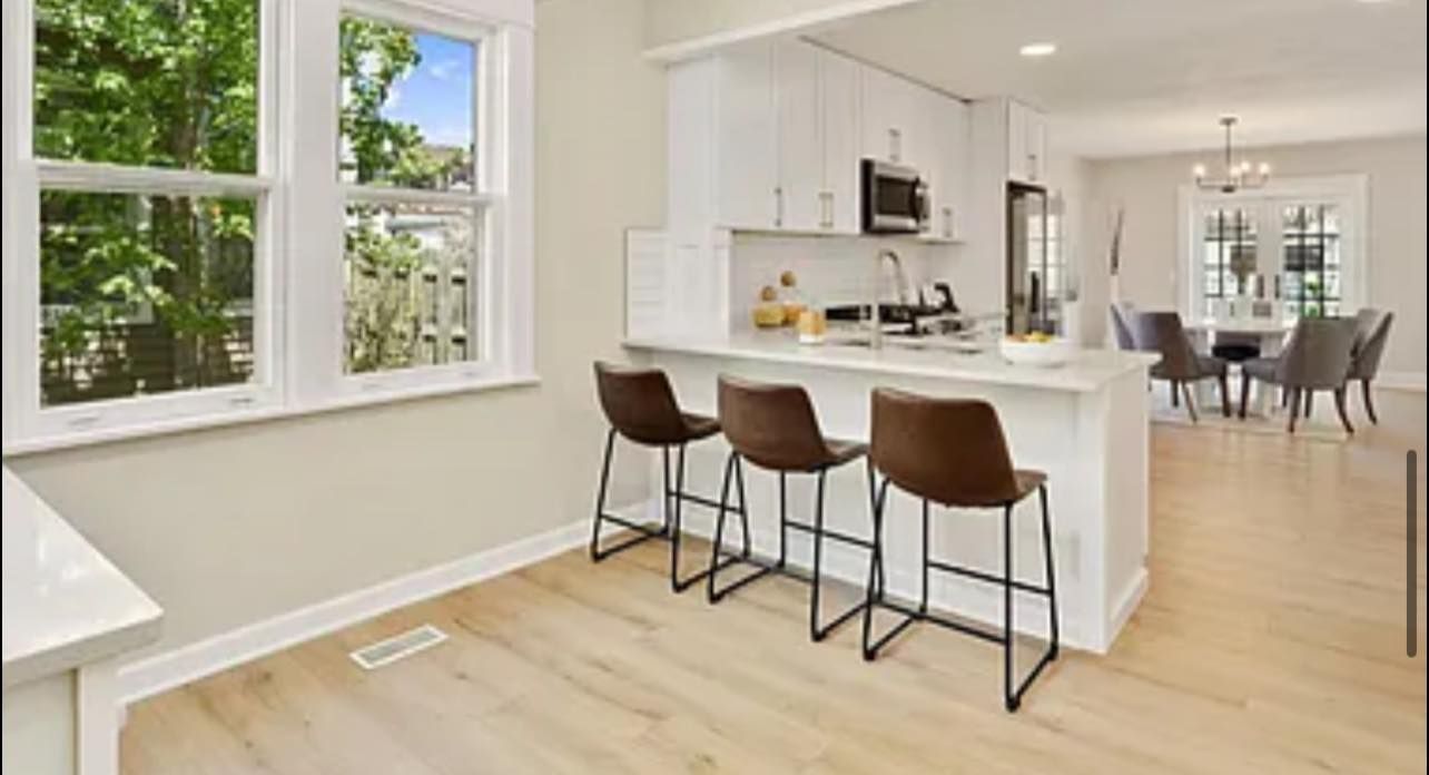 Kitchen with white cabinets, breakfast bar with stools, and dining area with a table and chairs.