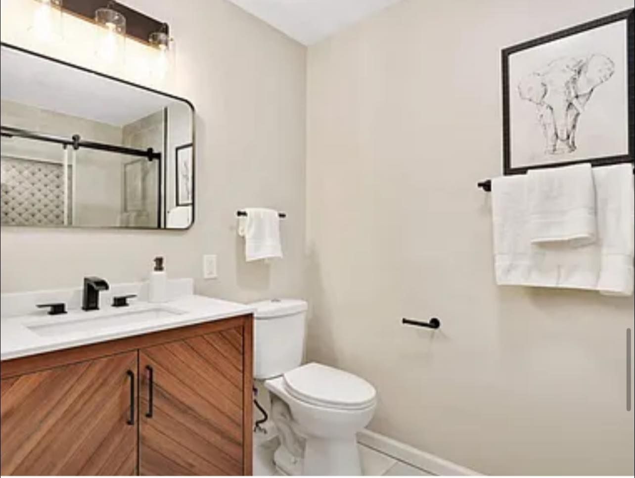 Bathroom with a wooden vanity, white toilet, and an elephant art print, all against beige walls.