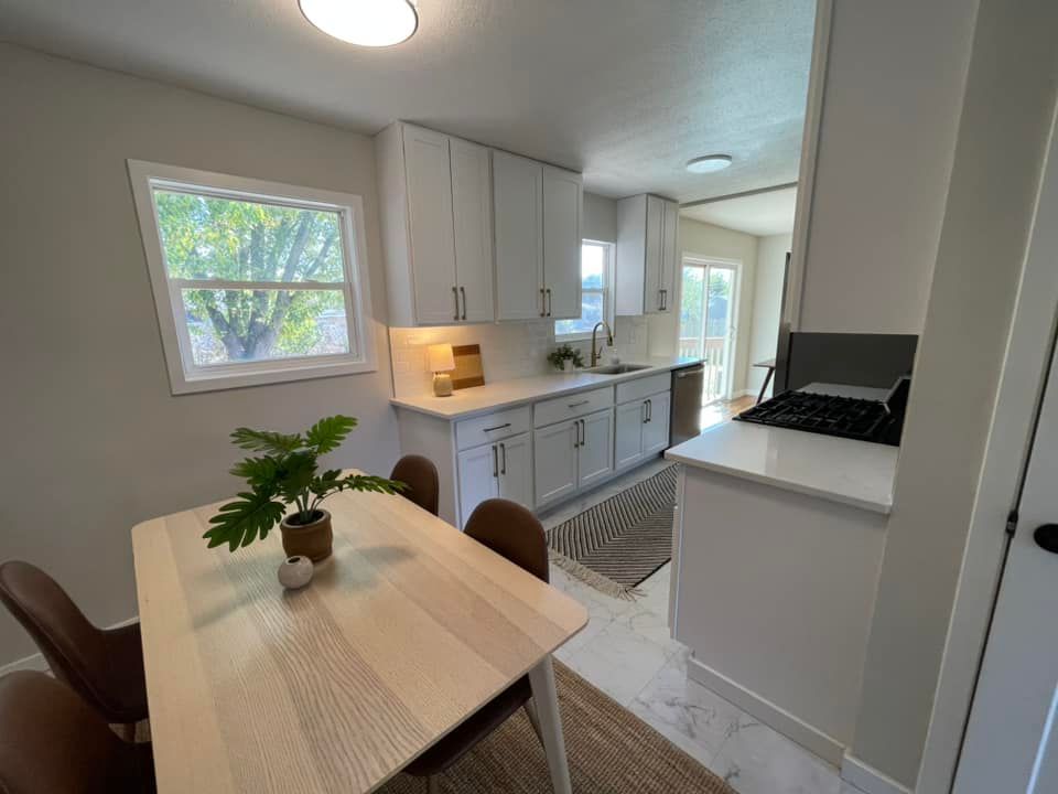 Modern kitchen with white cabinets, light wood table, and plant.