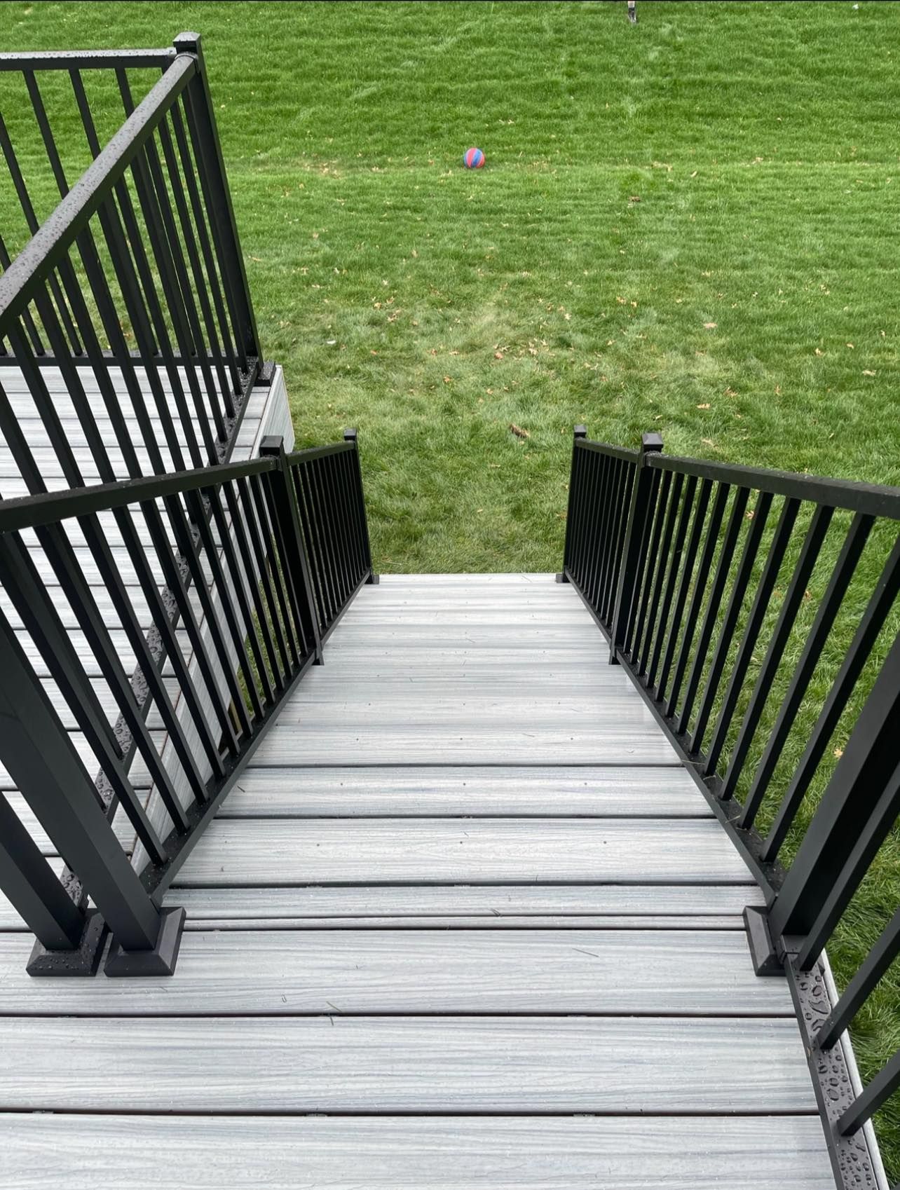 Gray deck stairs with black railings leading down to green grass.