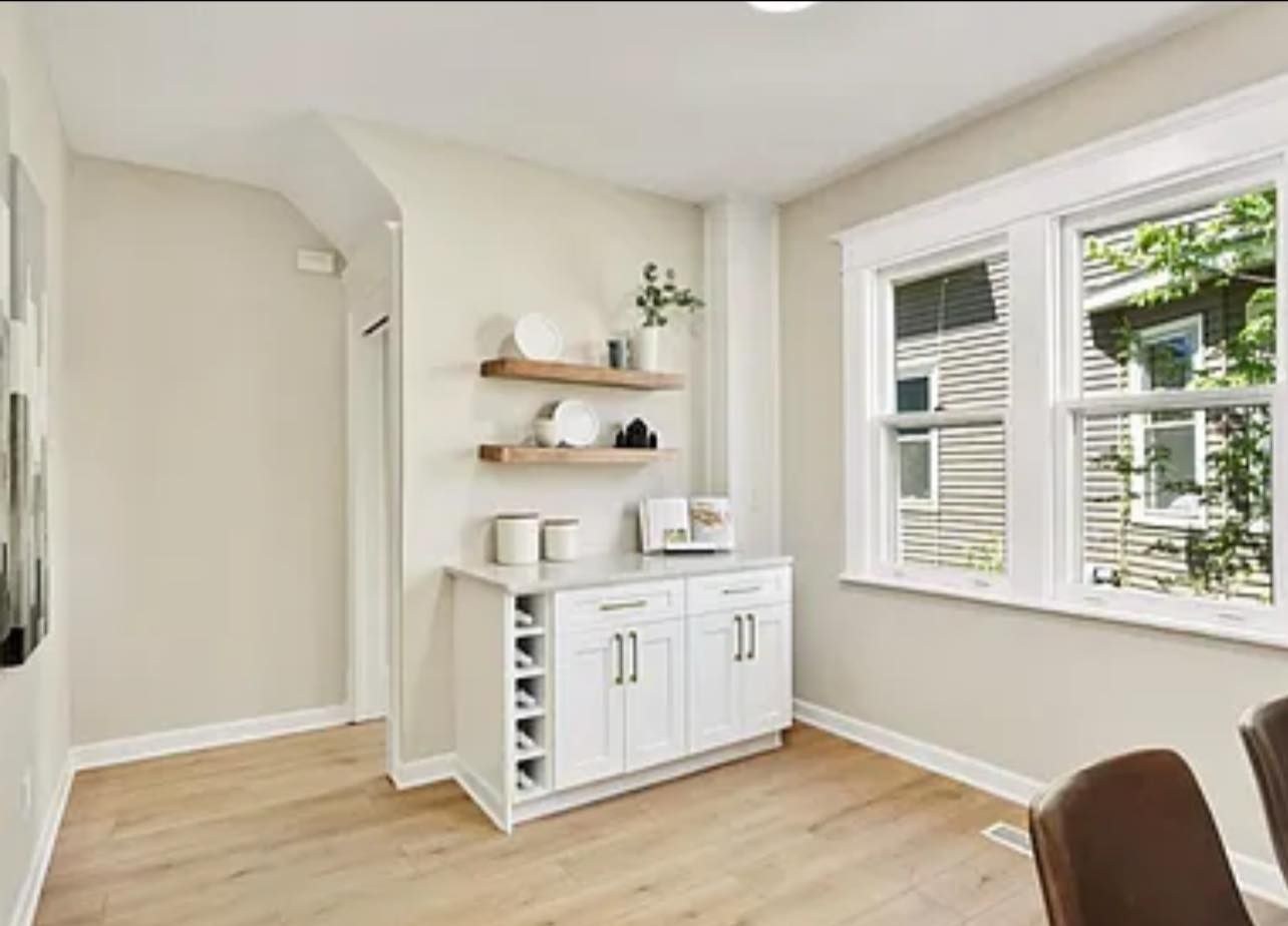 White built-in bar with shelves, wine rack, and window, set in a dining room with light wood floors.