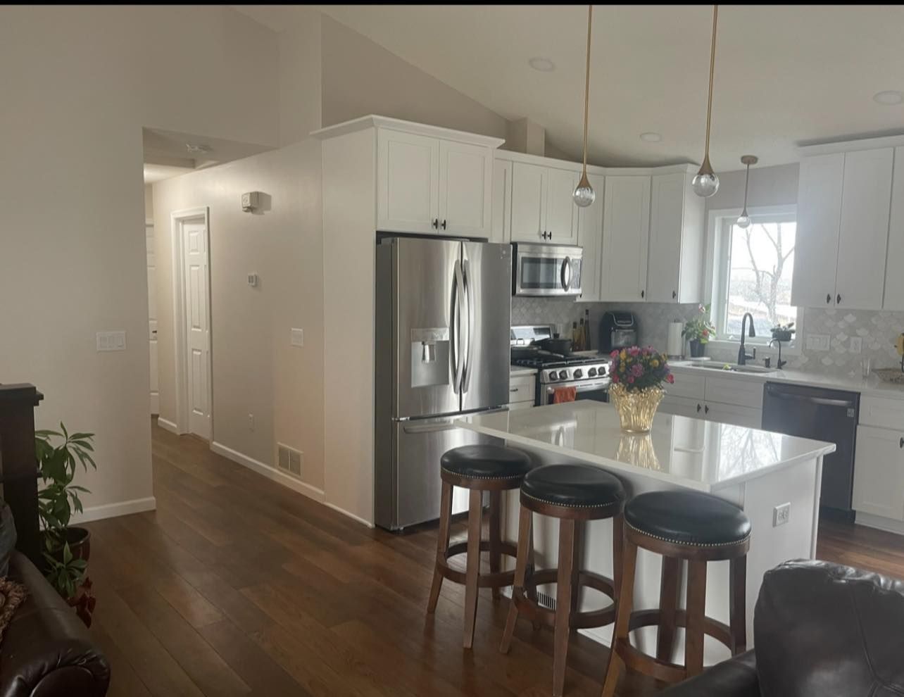 Modern white kitchen with stainless steel appliances, island seating, and wood floors.