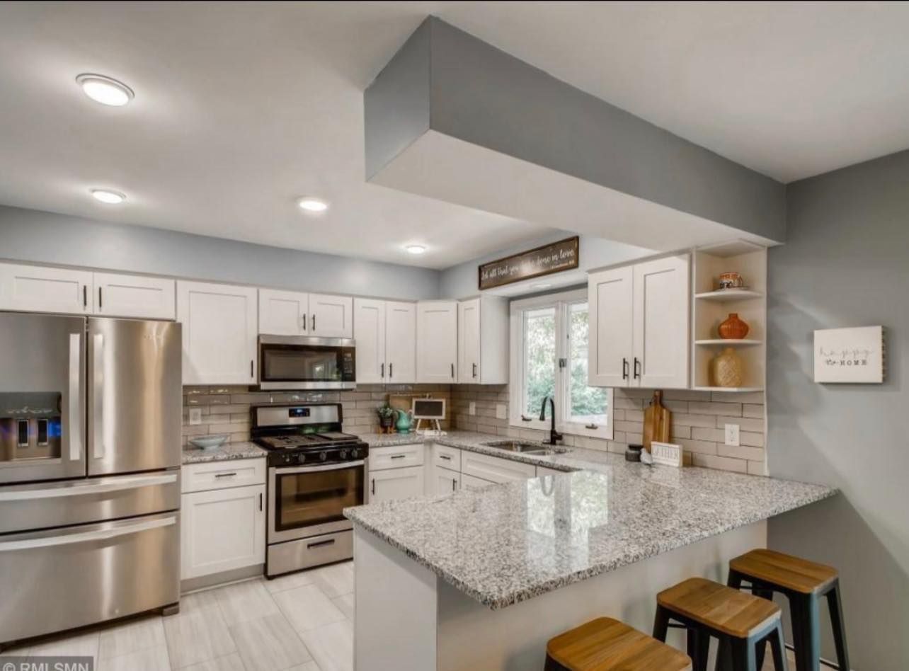 White kitchen with granite countertops, stainless steel appliances, and wood bar stools.