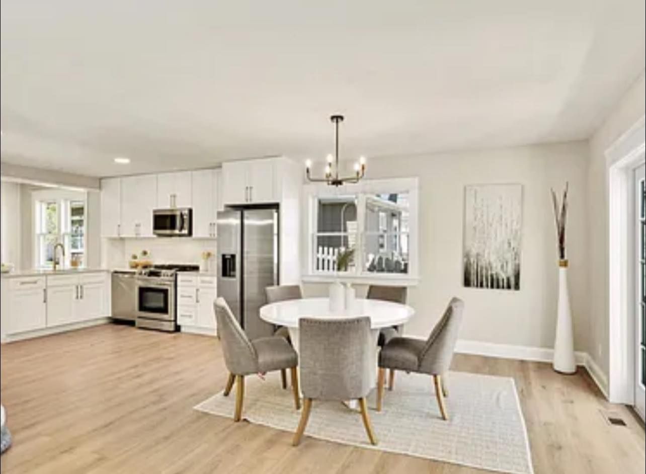 Open-concept kitchen and dining area with white cabinets, stainless steel appliances, round table, and light wood floors.