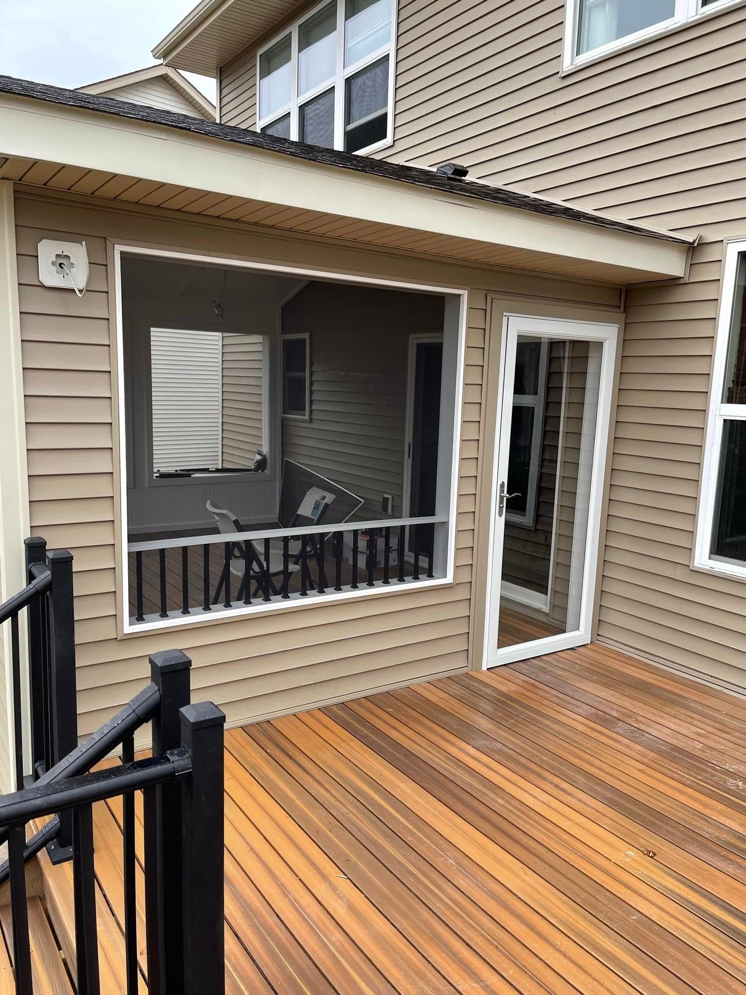 Screened porch with glass door and wooden deck; tan siding, black railing.