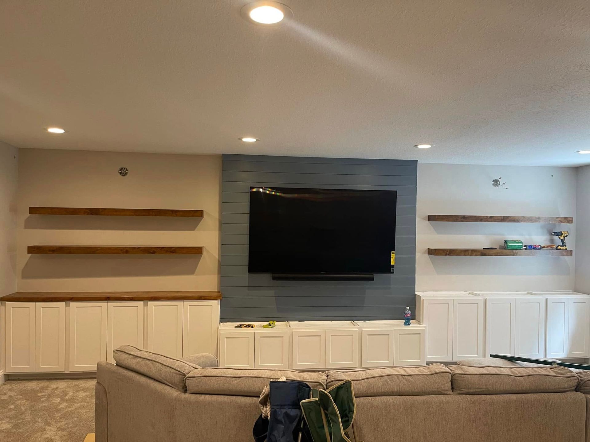 Living room with TV mounted on a blue accent wall, cabinets, and floating wooden shelves.