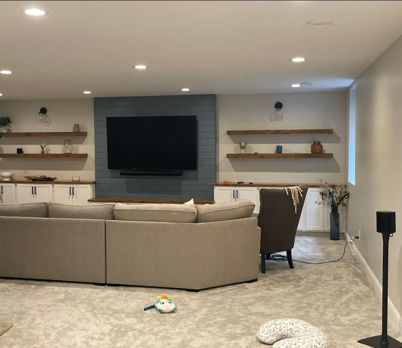 Living room with large sectional, TV on blue shiplap wall, floating shelves, built-in cabinets, and recessed lighting.