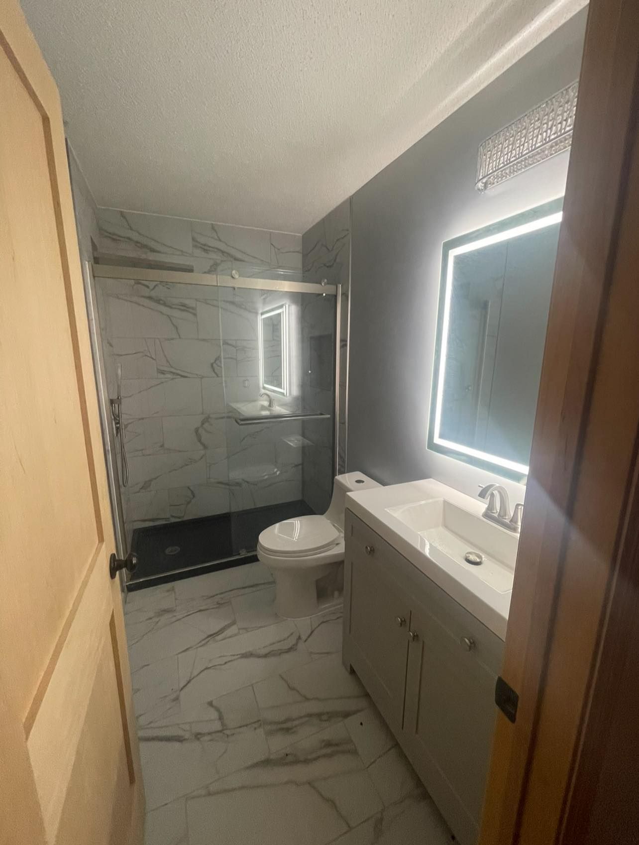 Modern bathroom with marble tile and gray walls; glass shower, vanity, and toilet.