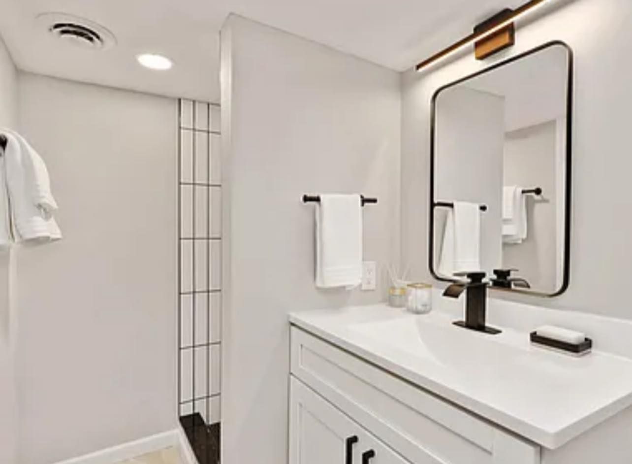 Bathroom with white vanity, black faucet, rectangular mirror, and shower stall.