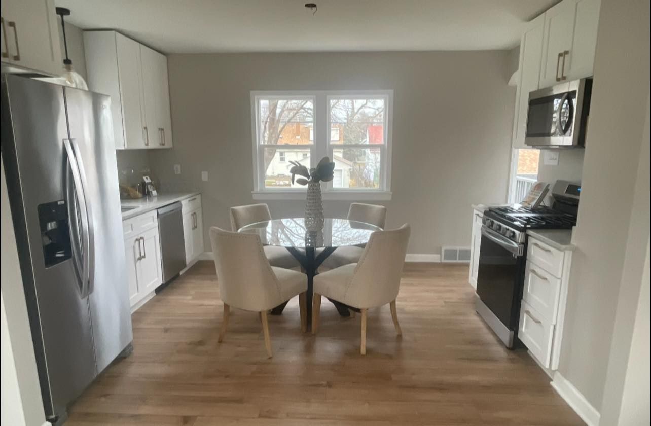 Kitchen with white cabinets, stainless steel appliances, table with chairs, and natural light.