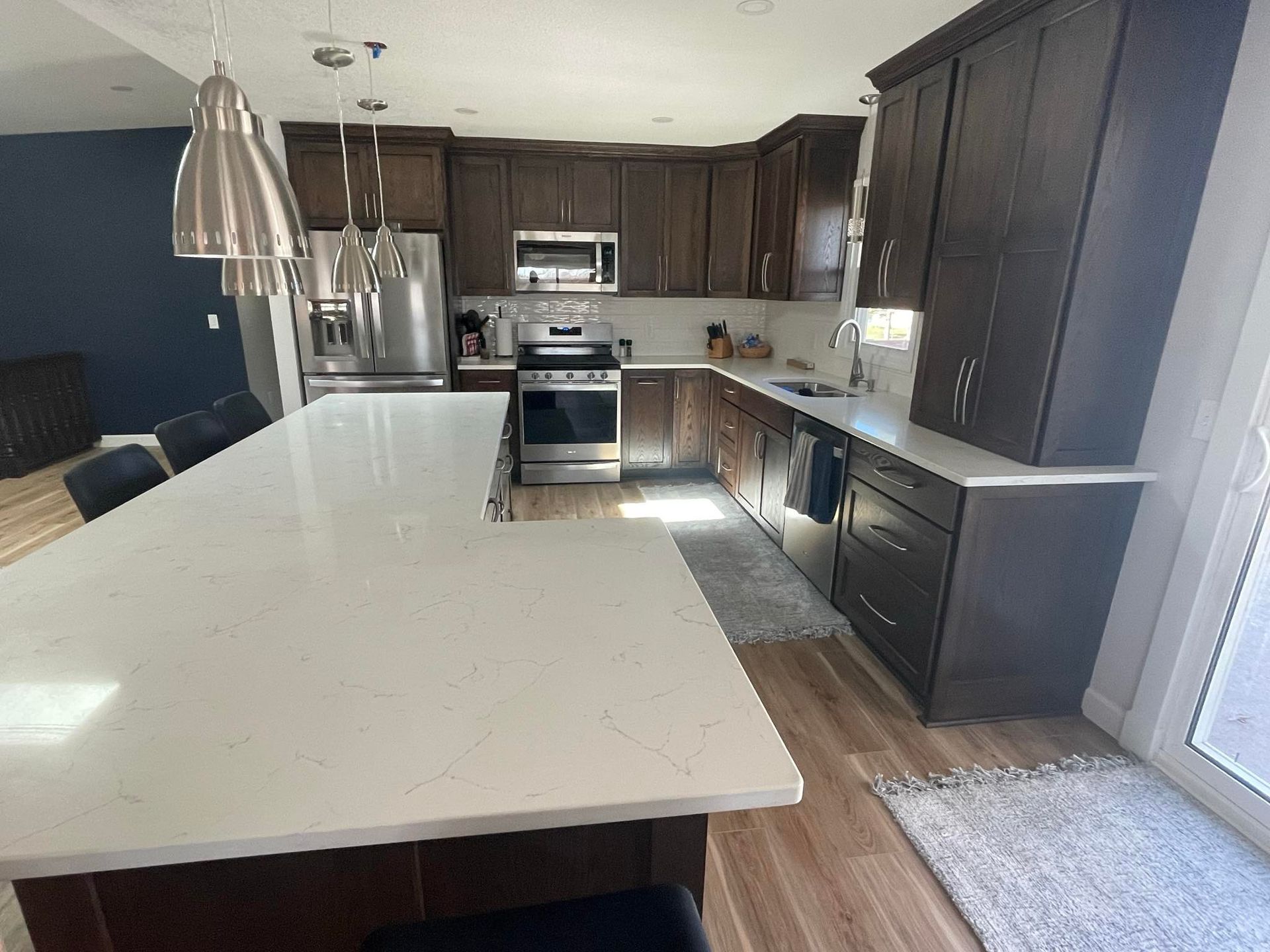 Modern kitchen with dark brown cabinets, white countertops, stainless steel appliances.