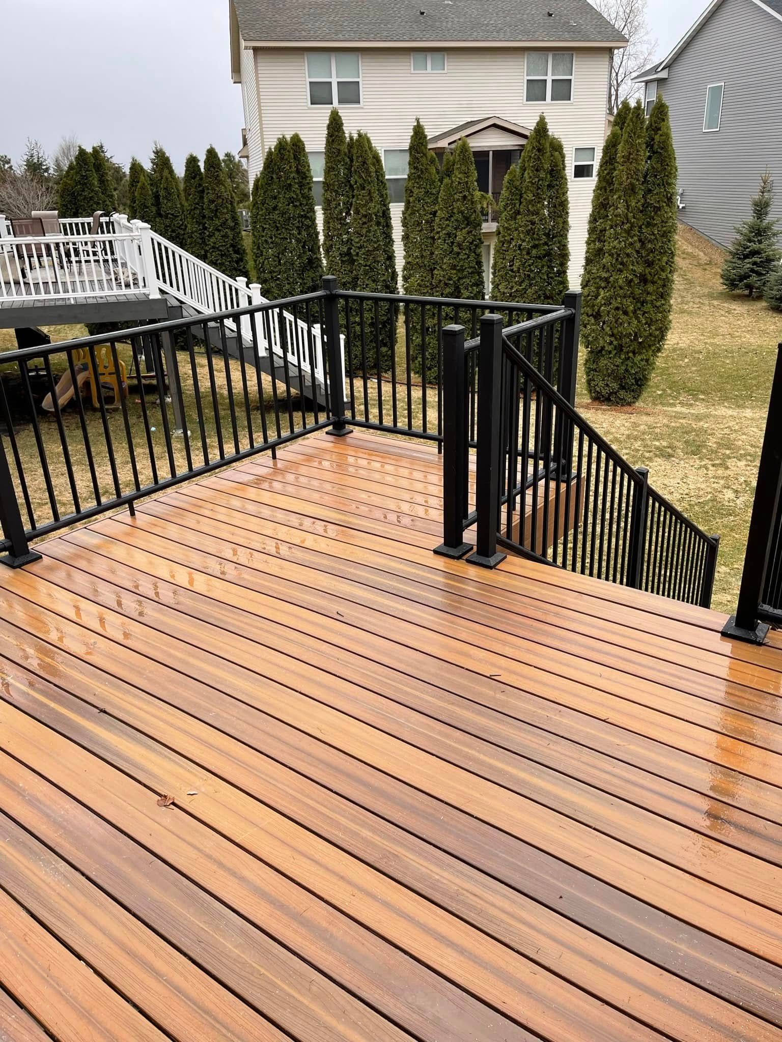 Brown wooden deck with black railings and stairs; a house in the background.