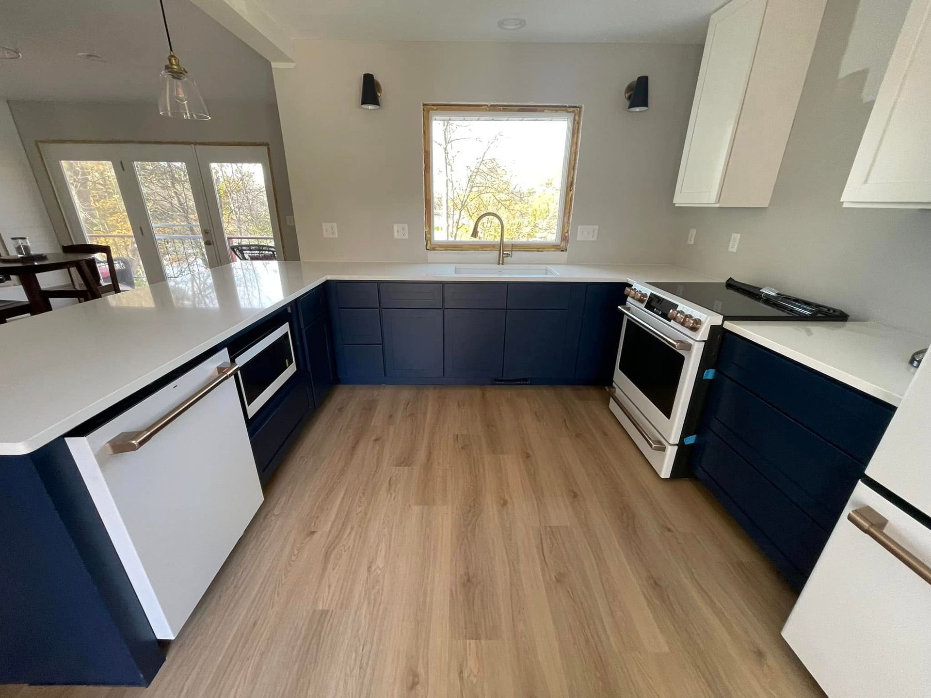 Modern kitchen with dark blue cabinets, white countertops, and wood-look flooring.