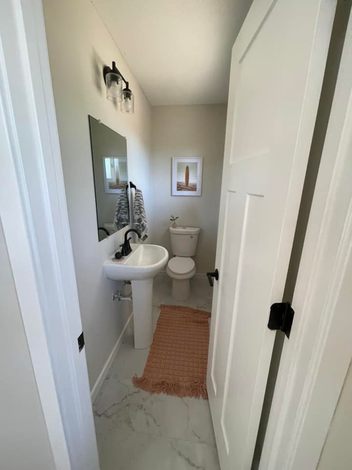 Small powder room with a white pedestal sink, toilet, and peach rug.