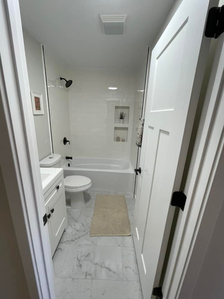 Small white bathroom with a tub, toilet, and vanity seen through a doorway.