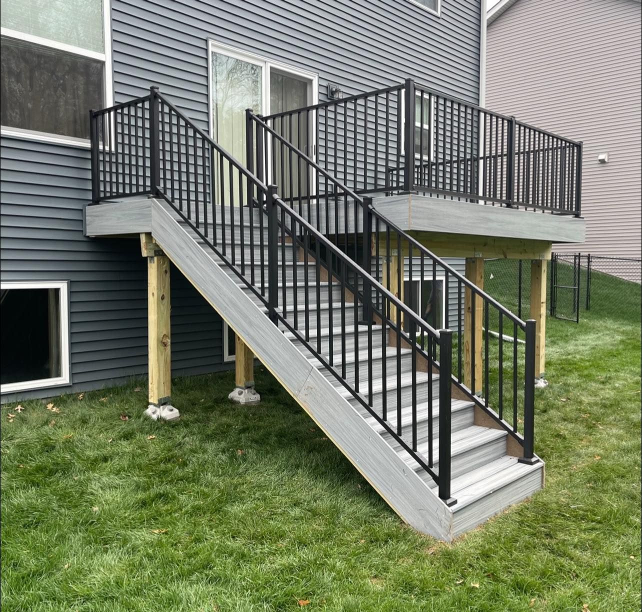 Deck with black railings and gray steps leading to a gray deck.  House with gray siding.