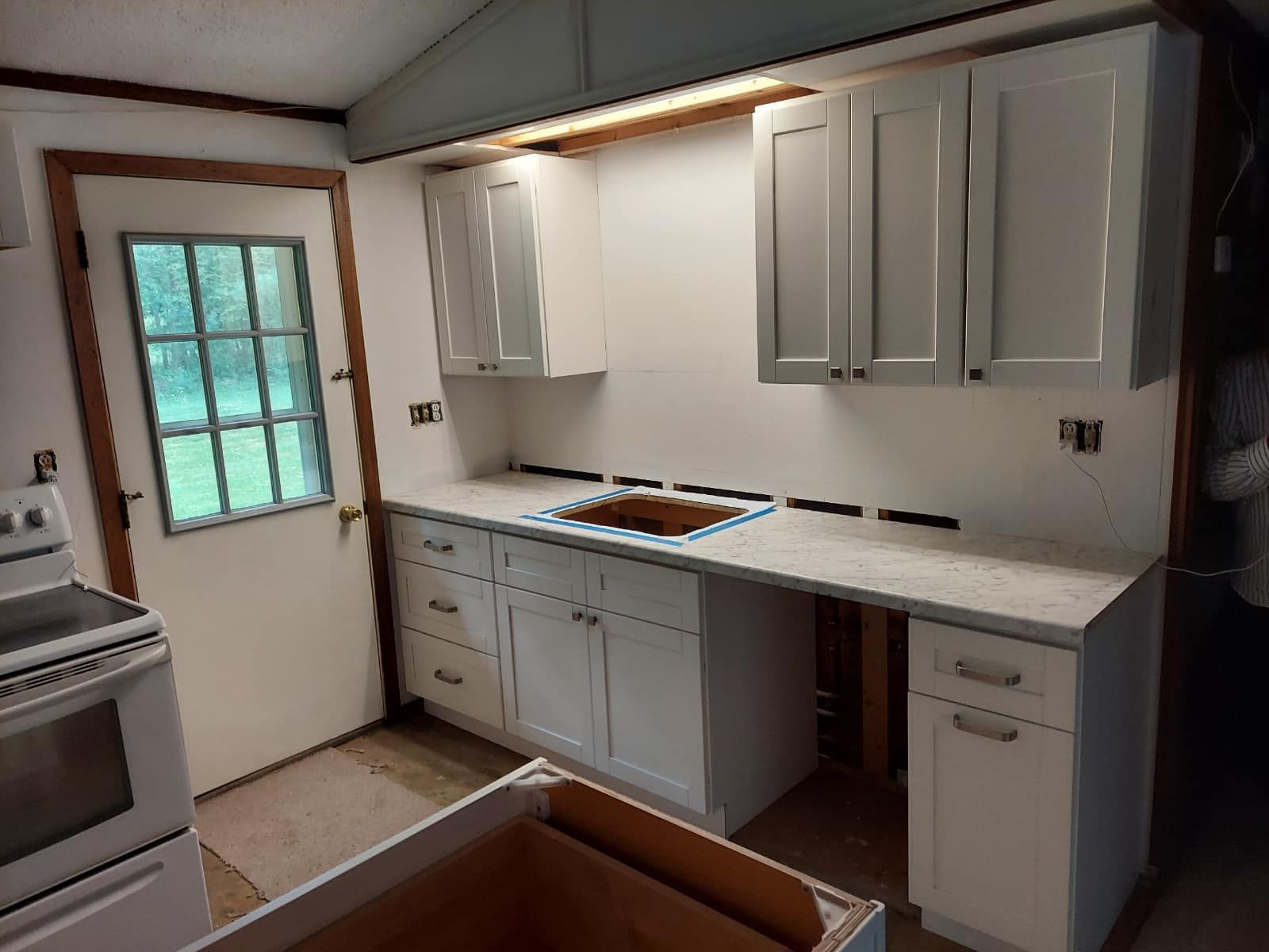 Newly installed kitchen cabinets with countertops. White and grey. Door and stove visible.