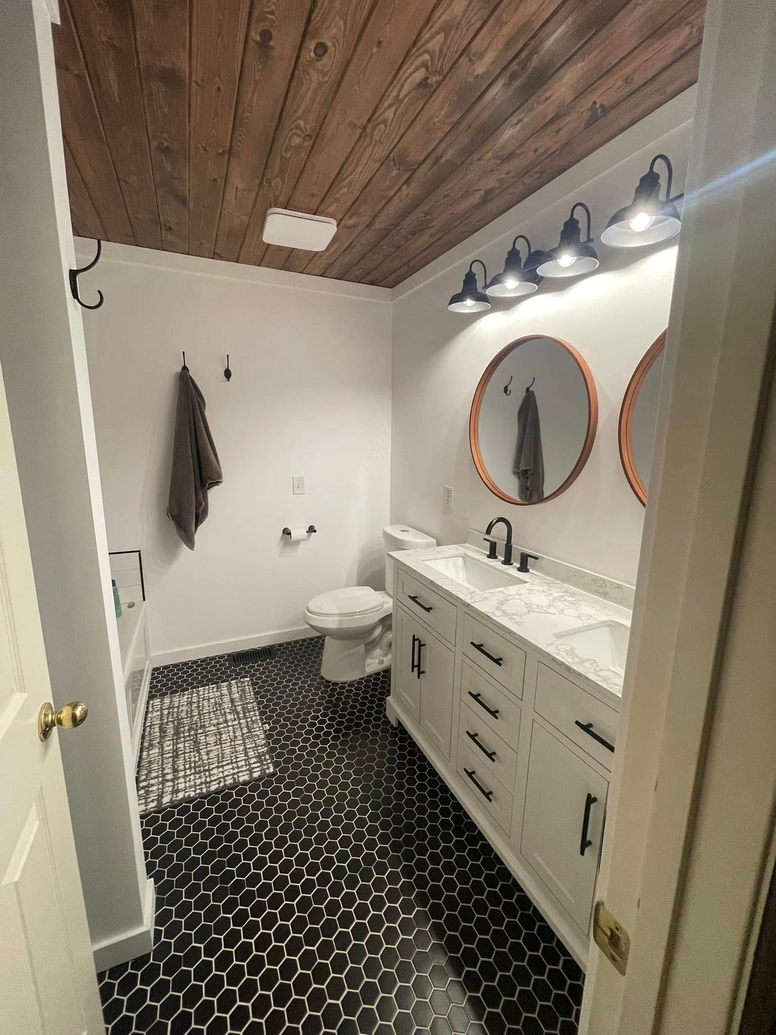 Bathroom with wooden ceiling, white vanity, black and white patterned floor, and round mirrors.