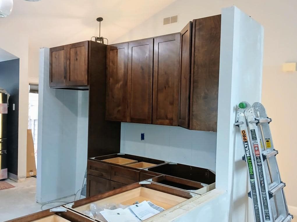Kitchen under construction with dark brown cabinets, unfinished base cabinets, and a ladder.