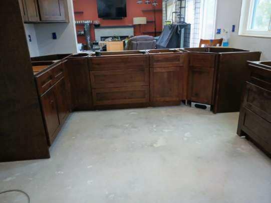 Kitchen cabinets in various stages of installation, dark wood, on a light concrete floor.