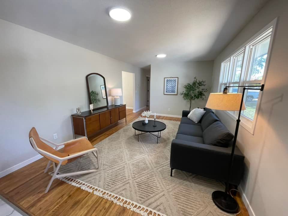 Living room with gray walls, wood floors, and neutral rug. Black couch, mid-century modern furniture, and white trim.