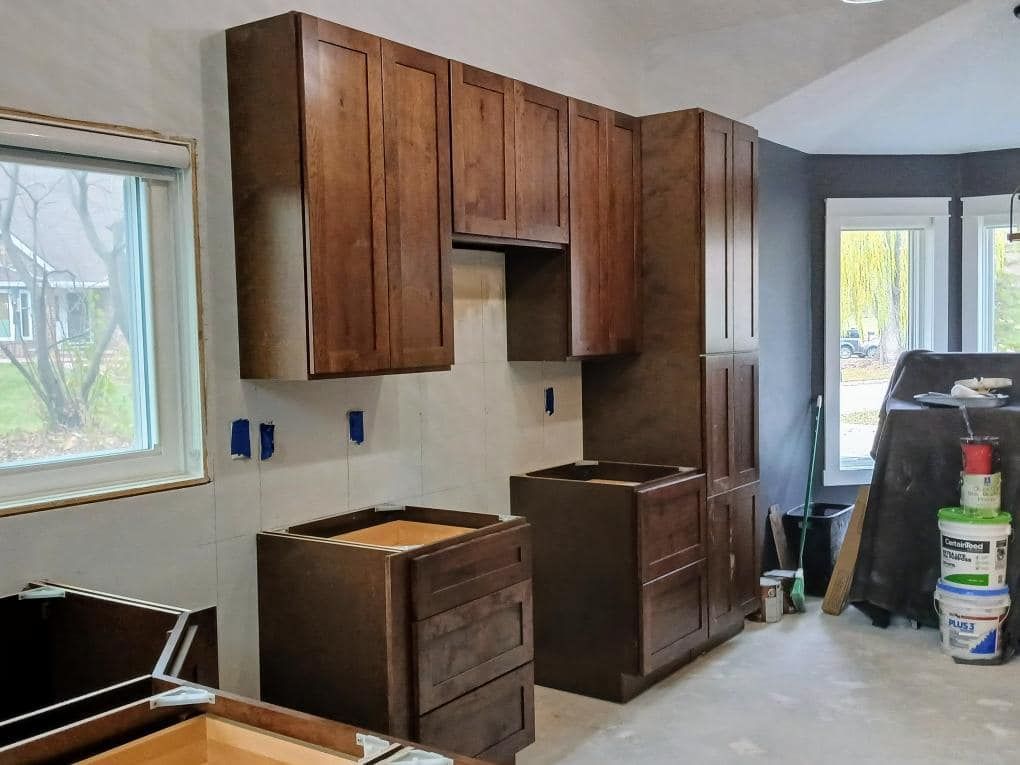 Kitchen cabinets being installed; brown wood cabinets on white and gray walls.
