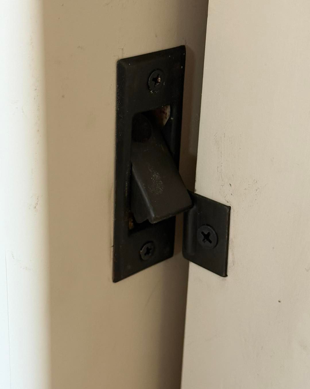 Black recessed pocket door pull and latch on white door and frame.