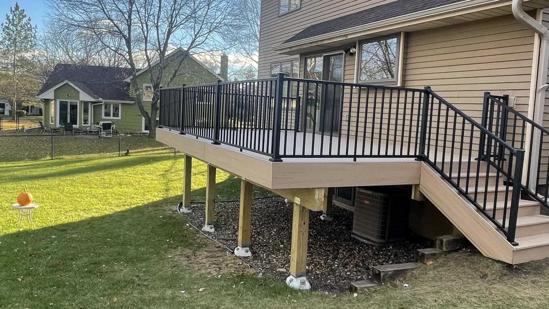 A multi-level deck attached to a house with black railings, tan decking, and stairs.